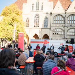 Hildesheimer Marktplatz mit Menschen die an Bierbänken sitzen und der Veranstaltung "Auf ein Wort mit Stephan Weil" zuhören.