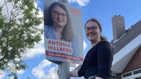 Antonia Hillberg steht auf einer Leiter und hängt ein Wahlplakat mit ihrem Foto an einer Laterne auf.
